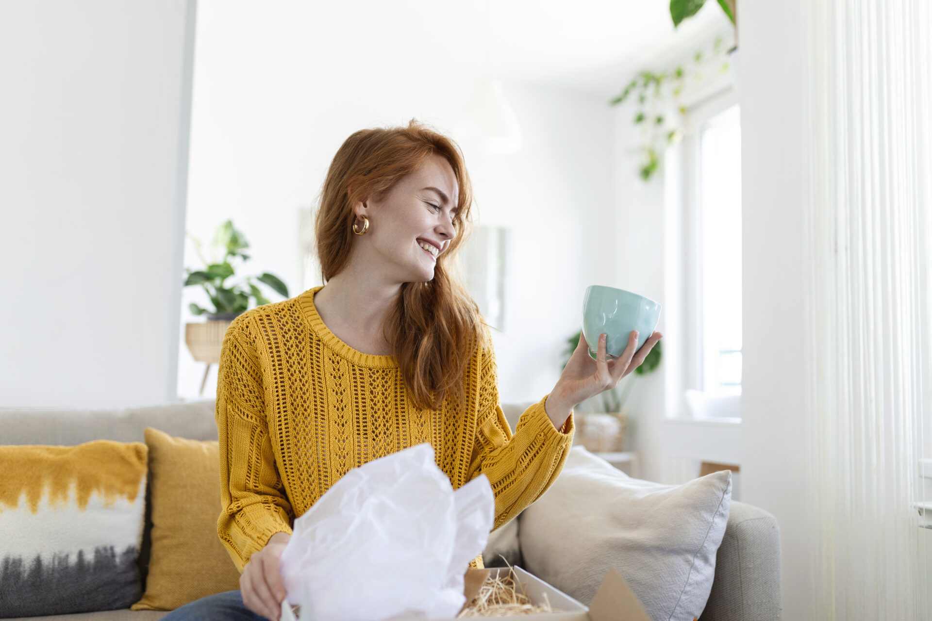 Smiling woman sit on couch at home open post package shopping online buying goods on internet, happy young female customer unpack postal shipping parcel satisfied with order or delivery